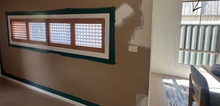 Wall with old tan paint, patched plaster and masking around a window