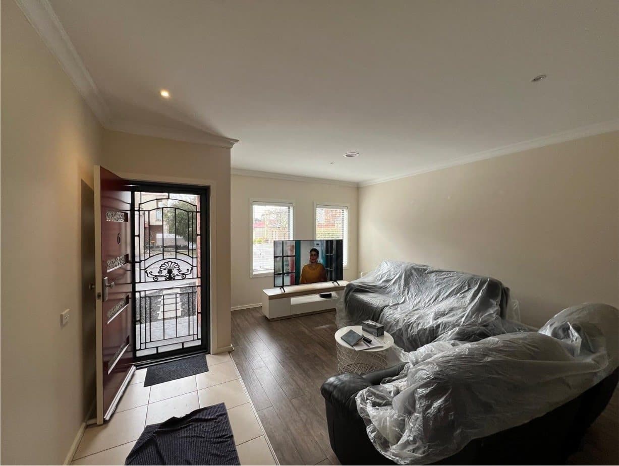Living room with beige walls and furniture wrapped in plastic ready for painting