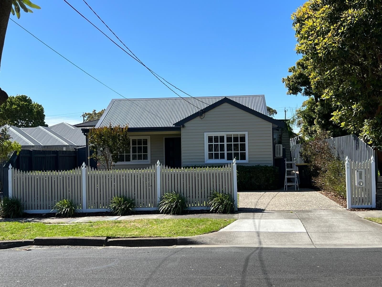 Weatherboard cottage with white picket fence and a ladder set up at the side