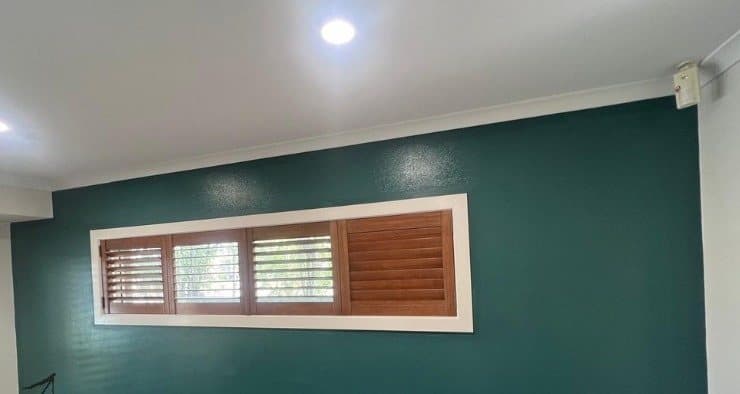 Finished deep green feature wall framing a timber shuttered window